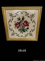 Frontal view of the framed needlepoint artwork showing pink roses and decorative border inside a gold frame.