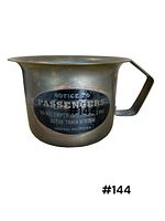 Small brass chamber pot with blue and white passenger notice decal, showing front and side profile with handle and spill spout