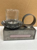 Photo showing a tin candle holder with a glass cup and a rectangular tin matches holder with pink strike strip