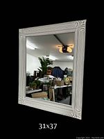 Rectangular white frame mirror with decorative carved patterns on frame, reflected room background, dimensions indicated as 31x37
