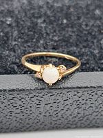 Close-up of 10K gold ring with round white opal center and side accents on black textured surface.