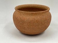 Profile view of the round, textured stoneware ceramic bowl showing its brown coarse exterior surface and curved shape.