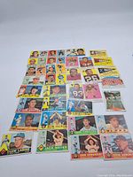 Top-down view of assortment of vintage sports cards laid out on a white surface, showing multiple rows of individual cards with various player portraits and designs.