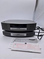 Front view of silver Bose Wave console stacked on multi-CD changer with user manual placed in front