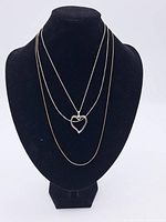 Three chains displayed on a black necklace bust, including a heart-shaped pendant.