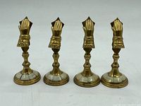 Front view of four brass place holders with finger-shaped clips, round bases with white inlay.