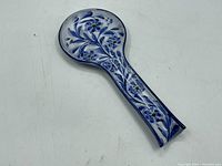 Top view of the spoon rest showing hand-painted blue flowers and green leaves on white ceramic with a glazed finish.