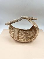 Front view showing the oval shape, natural weave pattern, and attached driftwood handle tied with twine.