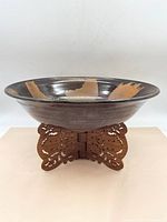 Front view of the large glazed ceramic bowl on the carved wooden base showcasing the bowl's pattern and shape.