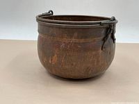 Copper pot shown from a side angle revealing worn patina and rounded shape with metal handles.