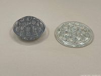 Two flower frogs displayed side by side, one clear and one smoky grey glass, showing front and top angles.