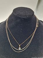 Three silver chains displayed on a black stand.