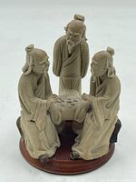 Front view of three ceramic elderly male figurines arranged around a small table on a wooden base.