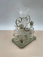 Front perspective of vintage condiment set with four glass containers and central cut glass vase on metal stand.