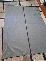 Full view of the large rectangular WW2 Canadian military wool blanket laid flat on a floor, showing the grey color and a black lengthwise stripe.