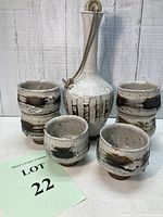 Photo showing ceramic sake decanter and six handmade cup set with speckled glaze and brush stroke accents, no damage visible.