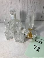 Five clear glass perfume bottles including hobnail, cut glass, low profile with tall stopper, and one with engraved motif, all grouped together on a surface with a lot number card.