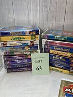 Photo showing the front and side views of various Disney VCR tapes in colorful original cardboard cases branded with titles and art for The Little Mermaid, Hercules, The Lion King, and others alongside two empty VCR movie holders.