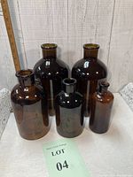 Five amber/brown glass apothecary bottles displayed against white wood background with a ruler showing approximate height.