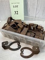 Image of plastic container holding multiple rusty iron shutter dogs with two displayed outside the container.