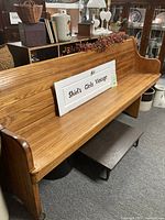 Long oak vintage church pew bench with curved seating area, light natural finish, displayed indoors among other vintage items.