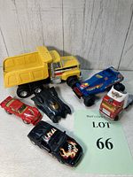 All five toy vehicles arranged on wooden floor against white paneled wall; metal dump truck, race cars and Batmobile visible