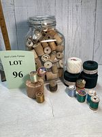 Jar filled with many vintage wooden thread spools, some empty and some with thread, displayed on wooden background surface
