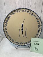 Full view of 12-inch diameter pizza plate with blue splatterware rim and central wheat motif on beige background on display stand.