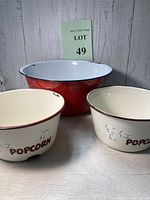 Three vintage enamel popcorn bowls: one large red and white with black trim, two smaller beige with brown trim and popcorn text.