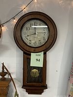 Full view of vintage wooden wall clock showing round face, glass front, wooden frame, lower pendulum cabinet.
