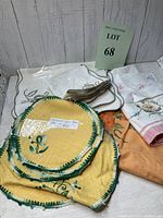 Overview of vintage linen placemats, napkins, and tablecloth pieces including yellow placemats with green edges, embroidered napkins, and folded linens in various colors.