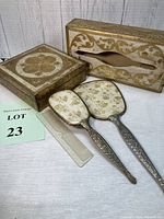 Photo showing two gold decorated wooden boxes, one tissue box holder with floral cutout, and one square box with gold floral lid, along with a matching gold floral vanity set: hand mirror, hairbrush, and clear comb.