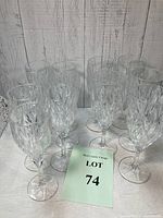 Front view of all 12 crystal glasses, 5 smaller and 7 larger, arranged together against a wood panel background.