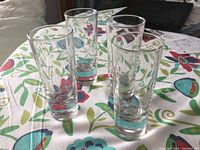 Four clear glasses with heavy bottoms arranged on a floral tablecloth.