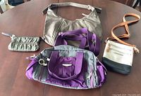 Four purses on a table: small cosmetic pouch, purple gym bag, small beige/black/brown shoulder bag, khaki shoulder bag