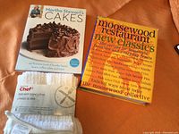 Photo showing two cookbooks and a pack of white bar mop dishcloths lying on a brownish/orange fabric surface.