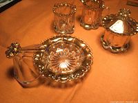 Butter dish with lid, spooner, sugar and creamer placed on orange cloth