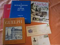 Four books about Guelph history with two commemorative first day postal covers laid on a surface