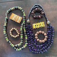 Full view of all 7 pieces showing necklaces and bracelets arranged on dark surface.