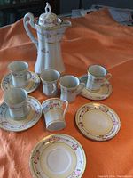 Full set of Nippon cocoa pitcher, six mugs, and five saucers arranged on orange fabric.