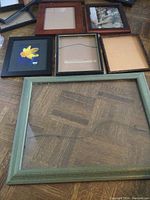Six assorted picture frames arranged on wood floor, varying sizes and conditions visible