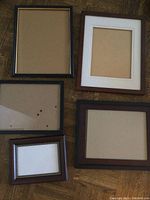 Five picture frames laid out on a wood floor showing different sizes and finishes, with paper backing inside.