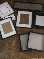 Various black-framed picture frames with matting including deep jersey display frames laid on wood floor.