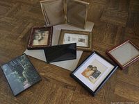 Full view of six picture frames on the floor showing different colors and styles including gold ornate, black, deep red wood, and clear glass hinge pair