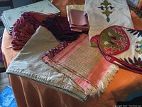 Photo shows various linen napkins in multiple colors, embroidered runners, and a woven runner on an orange surface.