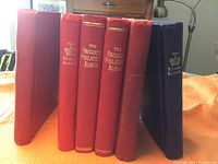 Six hardbound stamp albums in red and blue showing spines with gold-embossed titles