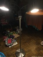 Full view of a silver metal floor lamp with two black lamp heads on flexible arms illuminated in a dim room.