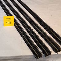 Four groups of black Atlas model train tracks laid out, each group with 5 pieces, total of 20 straight tracks.