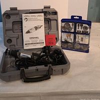 Dremel rotary tool inside gray plastic carrying case with instruction manual and accessory kit beside it.