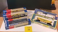 Front view showing five model railroad cars in boxes and blister packs including Walthers Gold Line and AHM on a wooden surface.